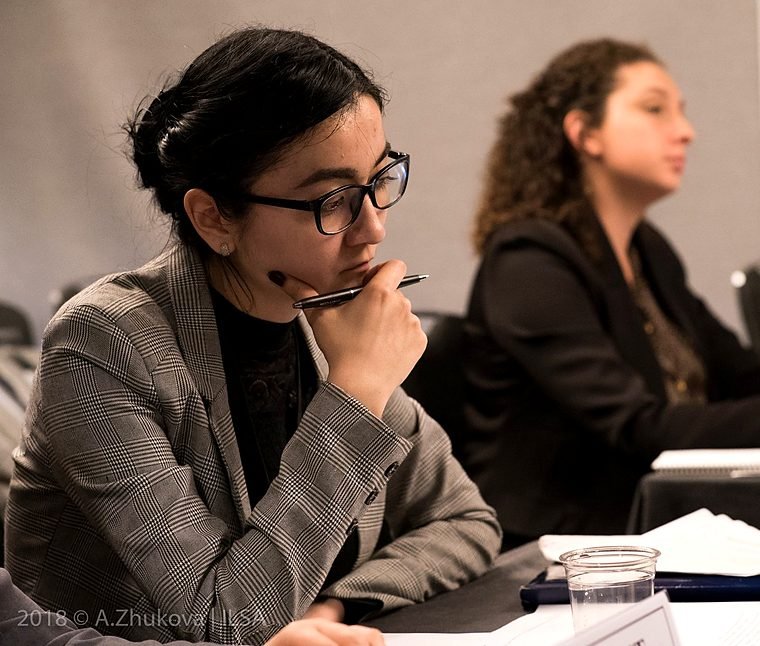 Two team members at a table during a round of the Jessup competition; one rests her chin on a pen, concentrating.