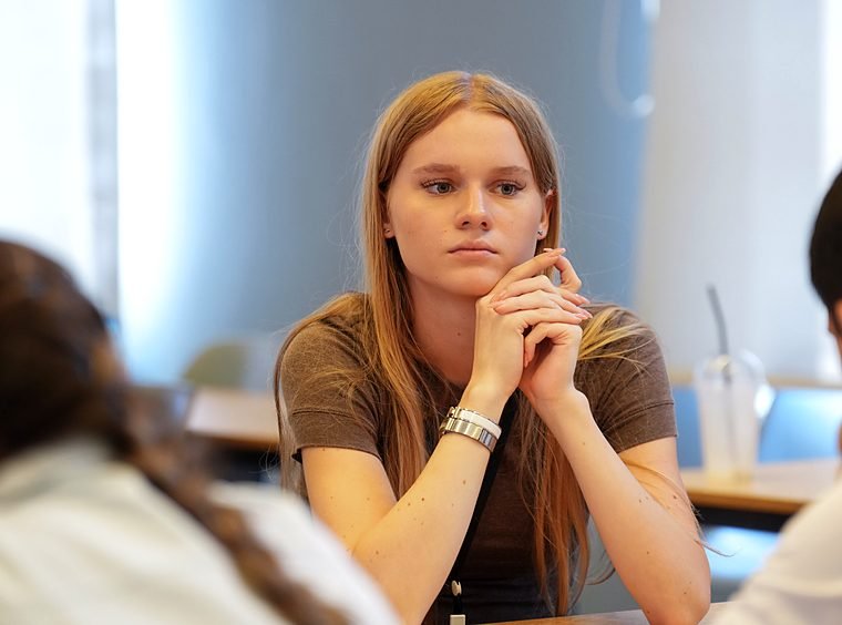 A student with her hands clasped listens thoughtfully during a session at the Summer School.