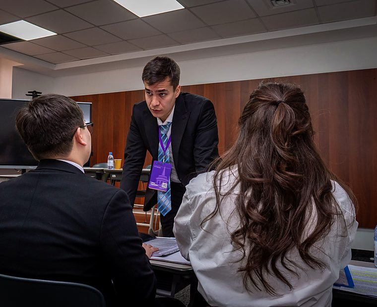 A coach leans in to speak with two team members at a table.