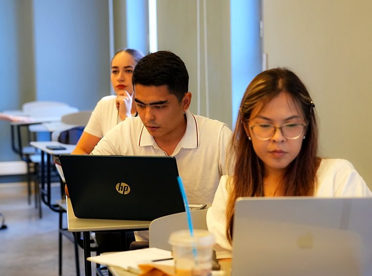 Two students work on laptops side by side at the Summer School.