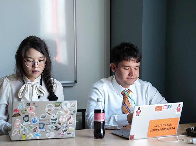 Two students with laptops work side by side at a table during a Summer School session.