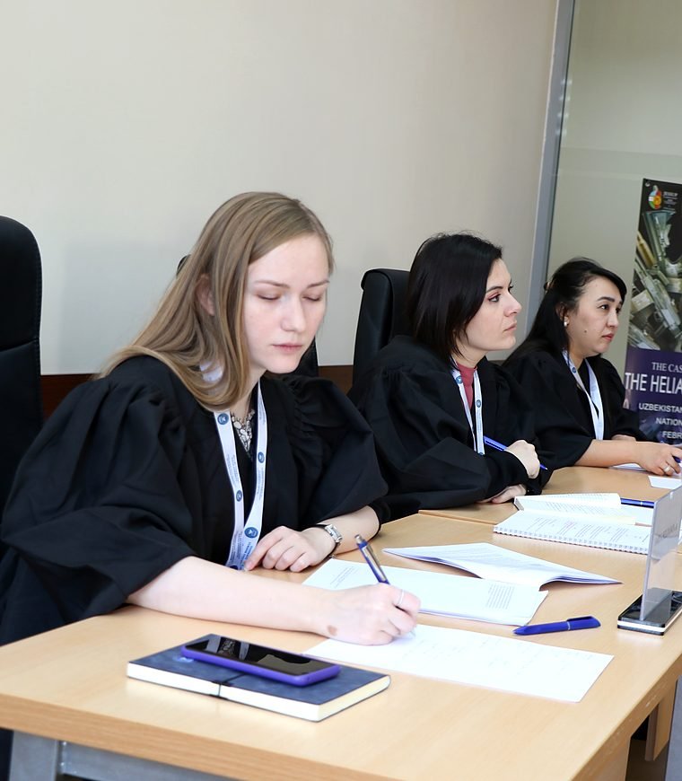 Three judges in black robes sit at the bench taking notes during a Jessup round.