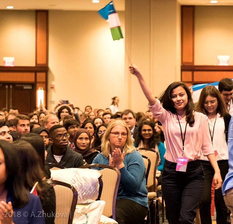 A student raises an arm holding the flag of Uzbekistan in a packed conference hall.