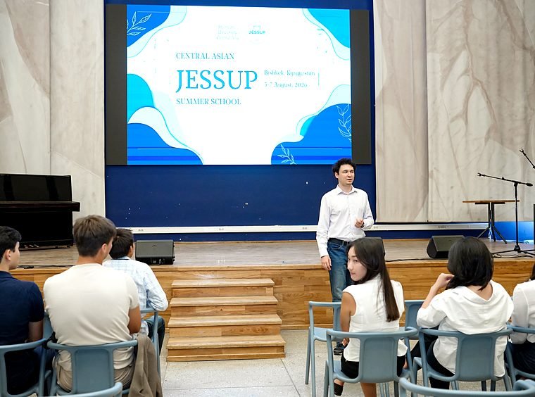 A speaker stands on stage in front of a screen reading "Central Asian Jessup Summer School".