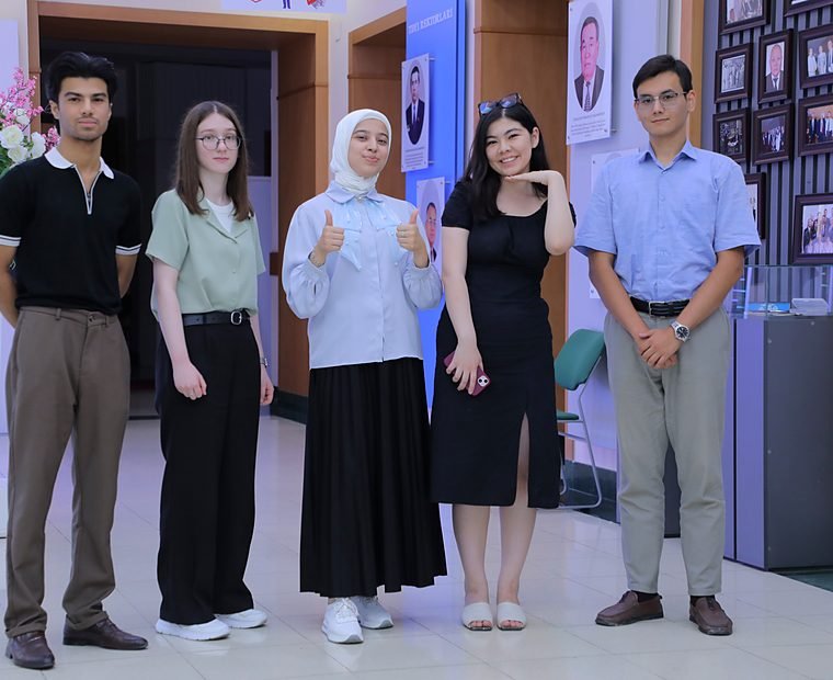 Five students stand together in a university lobby at the Summer School, smiling, two of them giving a thumbs-up.